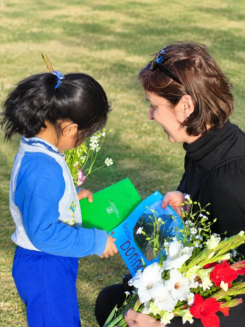 Donna receiving a thank-you card and flowers from a young student outdoors